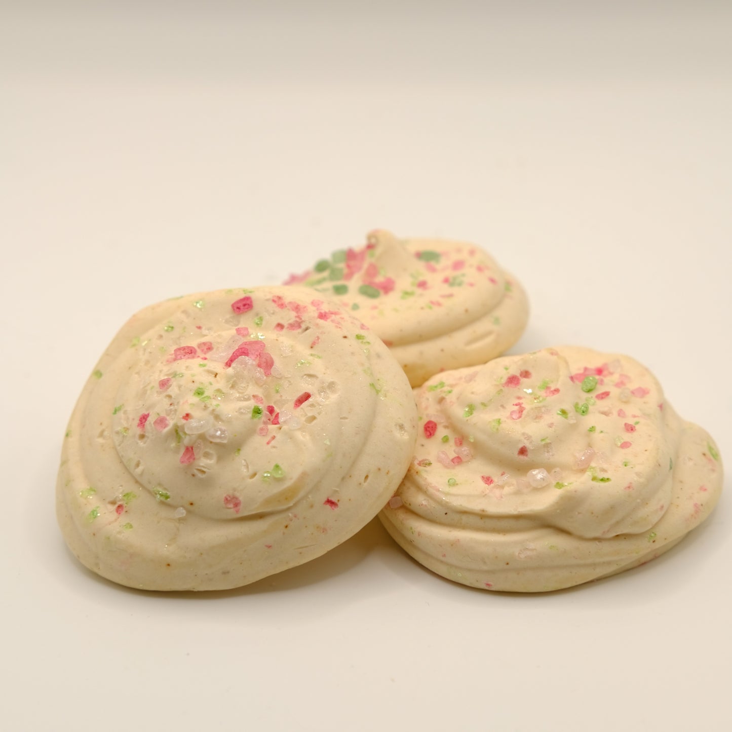 Three sugar cookies made out of soap with colorful sprinkles on a beige background