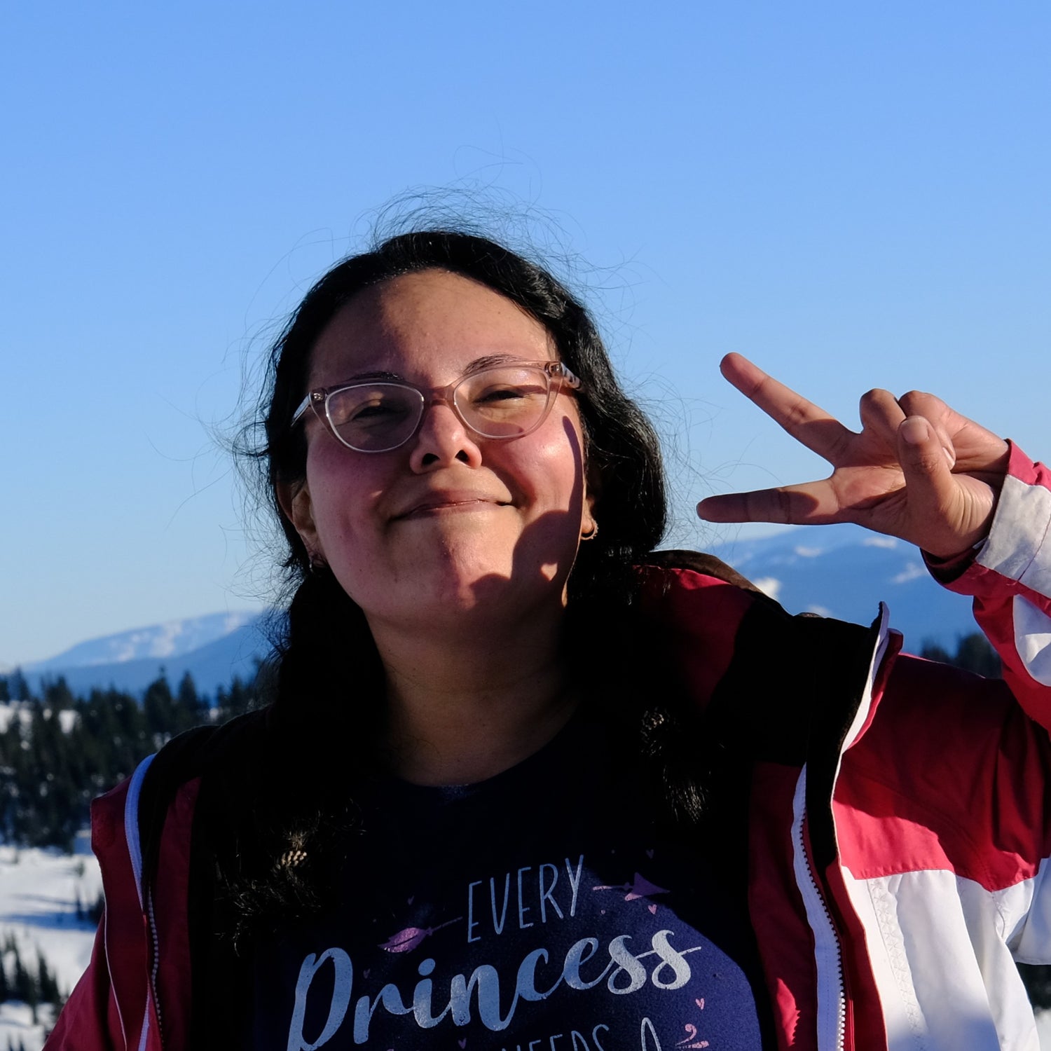 Person making a peace sign with their hand outdoors against a mountainous background