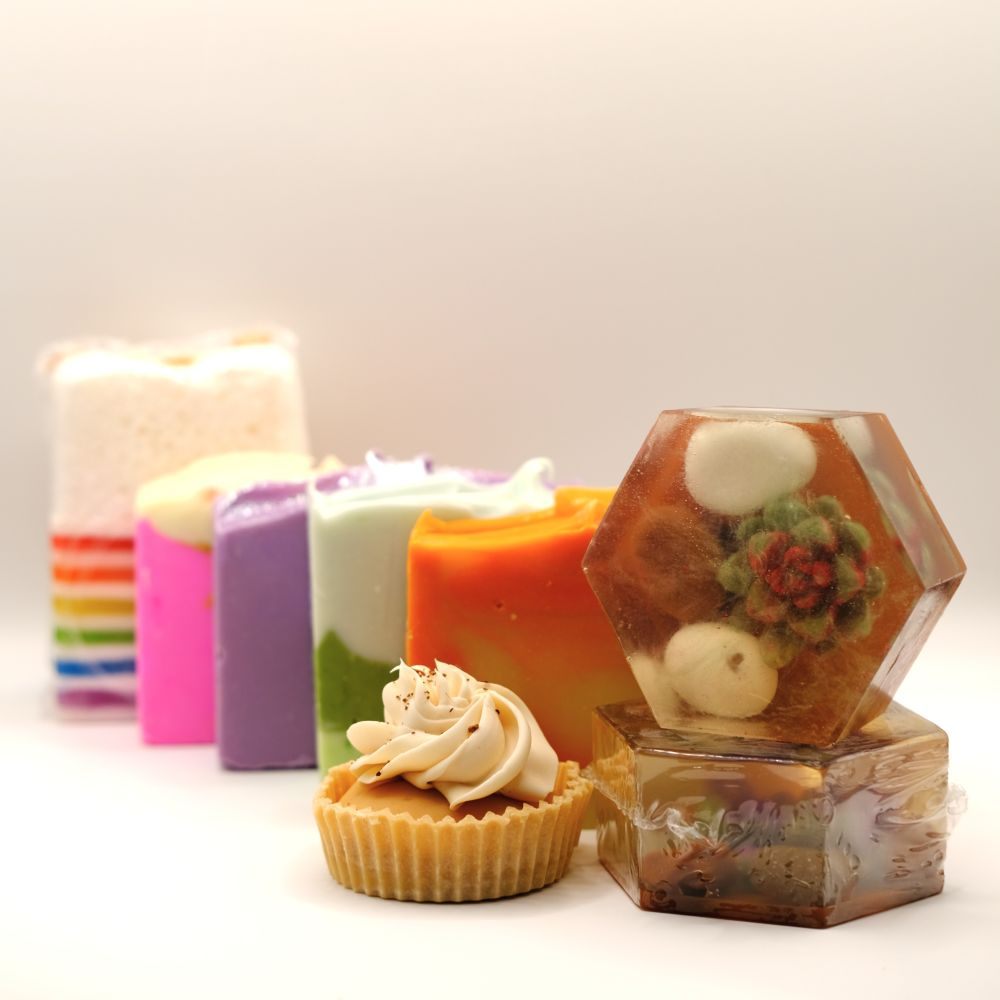 Assorted Soaps including a cupcake-shaped soap, a succulent soap and colorful soaps on a light background.