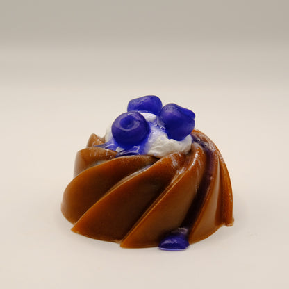 Bundt cake-shaped soap with blueberries, blue drizzle and white filling on a light gray background