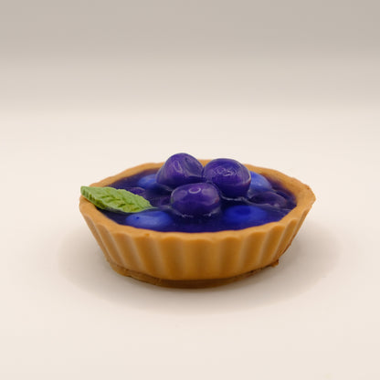 Small tart-shaped soap with blueberries and a mint leaf on a beige background