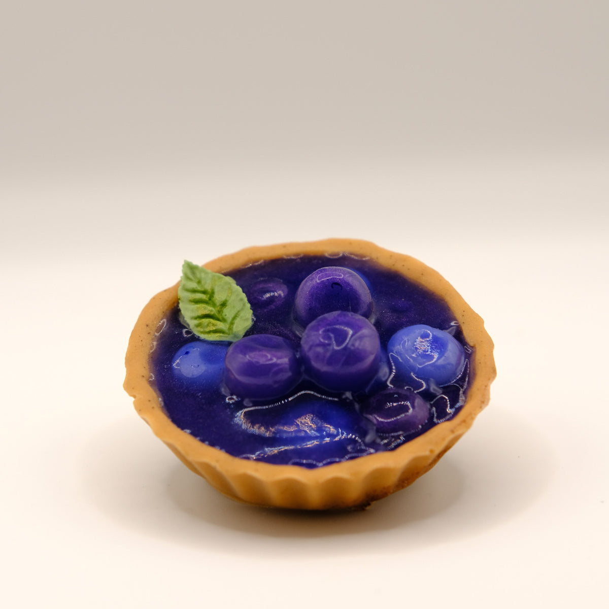 Small tart-shaped soap with blue fruit filling and a mint leaf design on a beige background