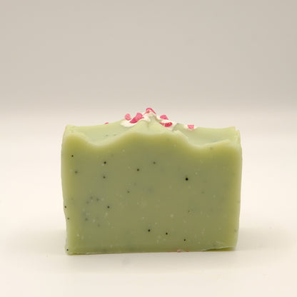 Green soap bar with specks and pink elements on a light gray background