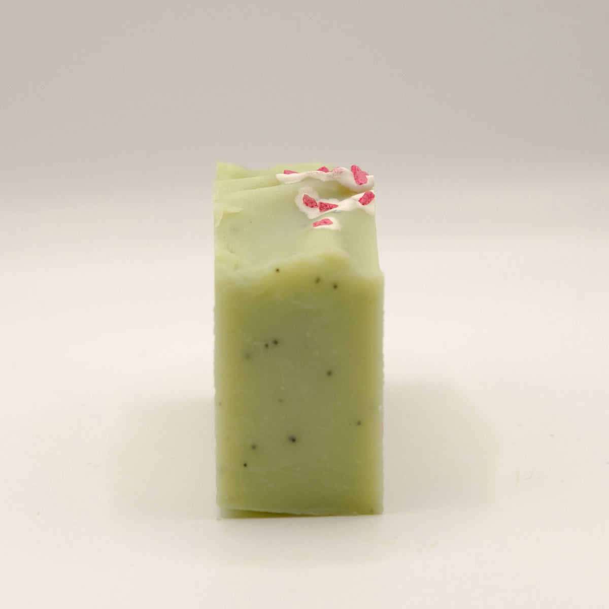 Green soap bar with pink specks on top and darker specks in the soap on a light gray background