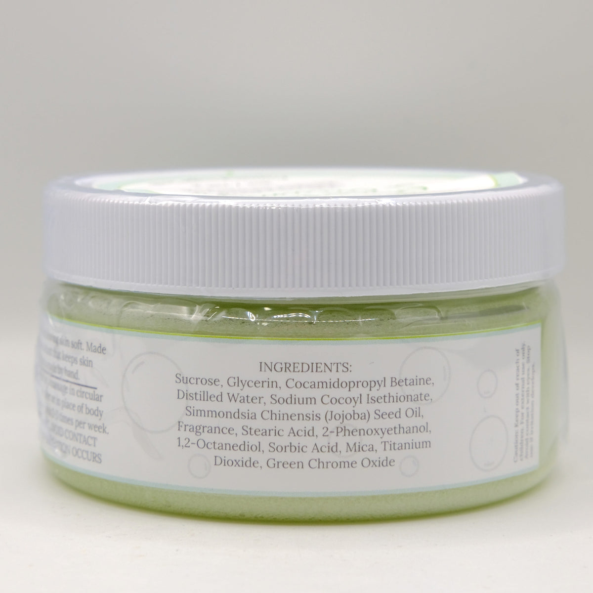 Jar of green sugar scrub with white lid on a light gray background