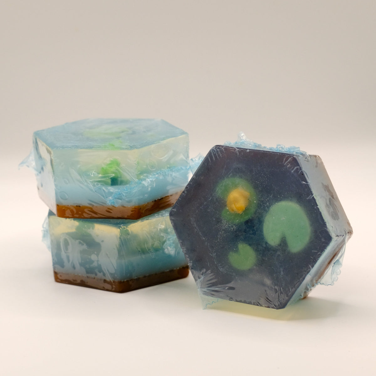Three hexagonal soap bars with mini frogs and lily pad design on a light gray background