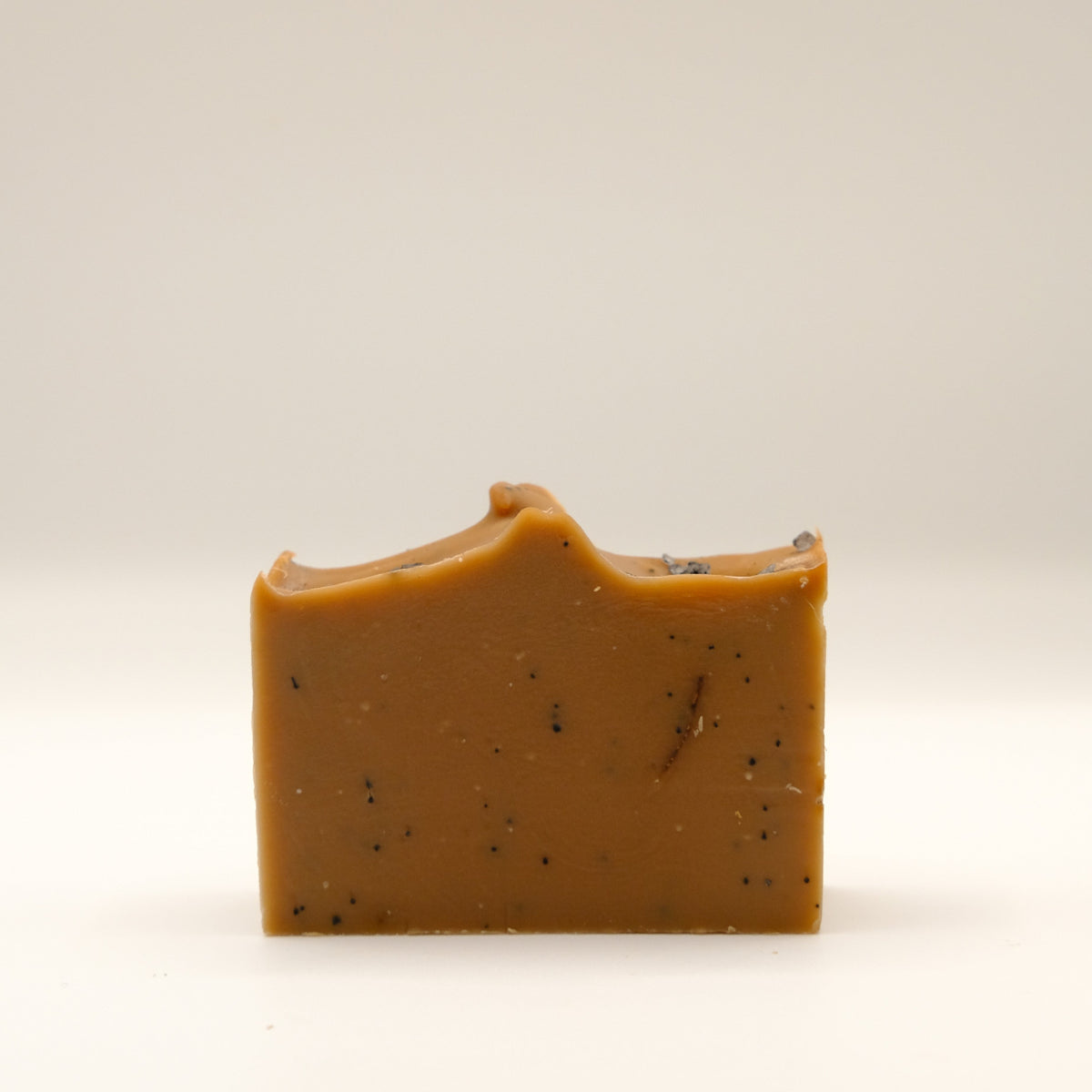 Brown bar of soap with specks and a textured top on a beige background