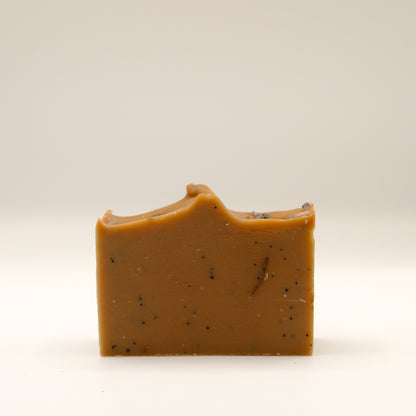 Brown bar of soap with specks and a textured top on a beige background