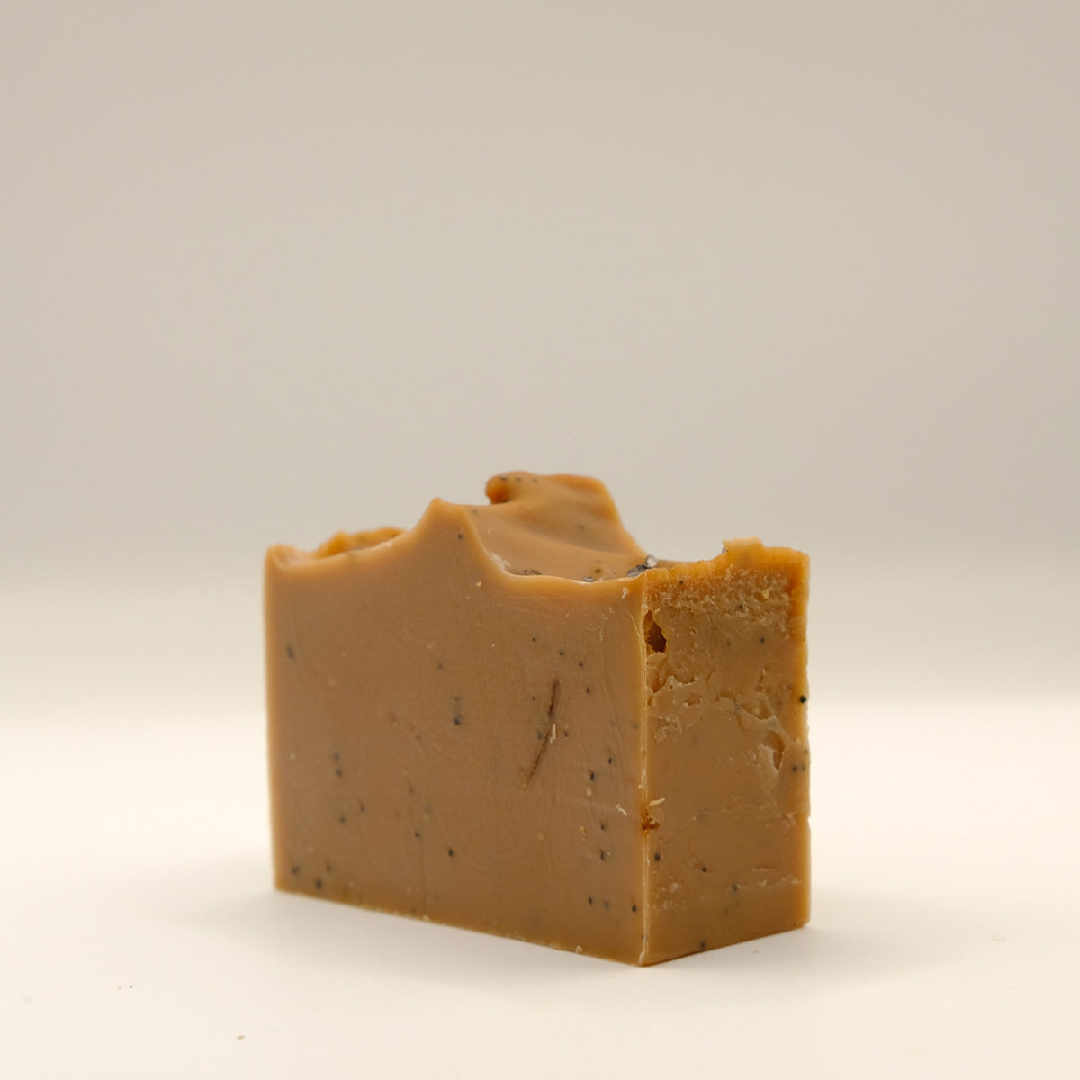 Bar of brown soap with specks and a textured top on a light gray background