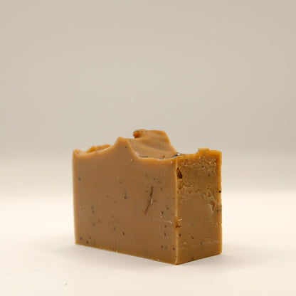 Bar of brown soap with specks and a textured top on a light gray background