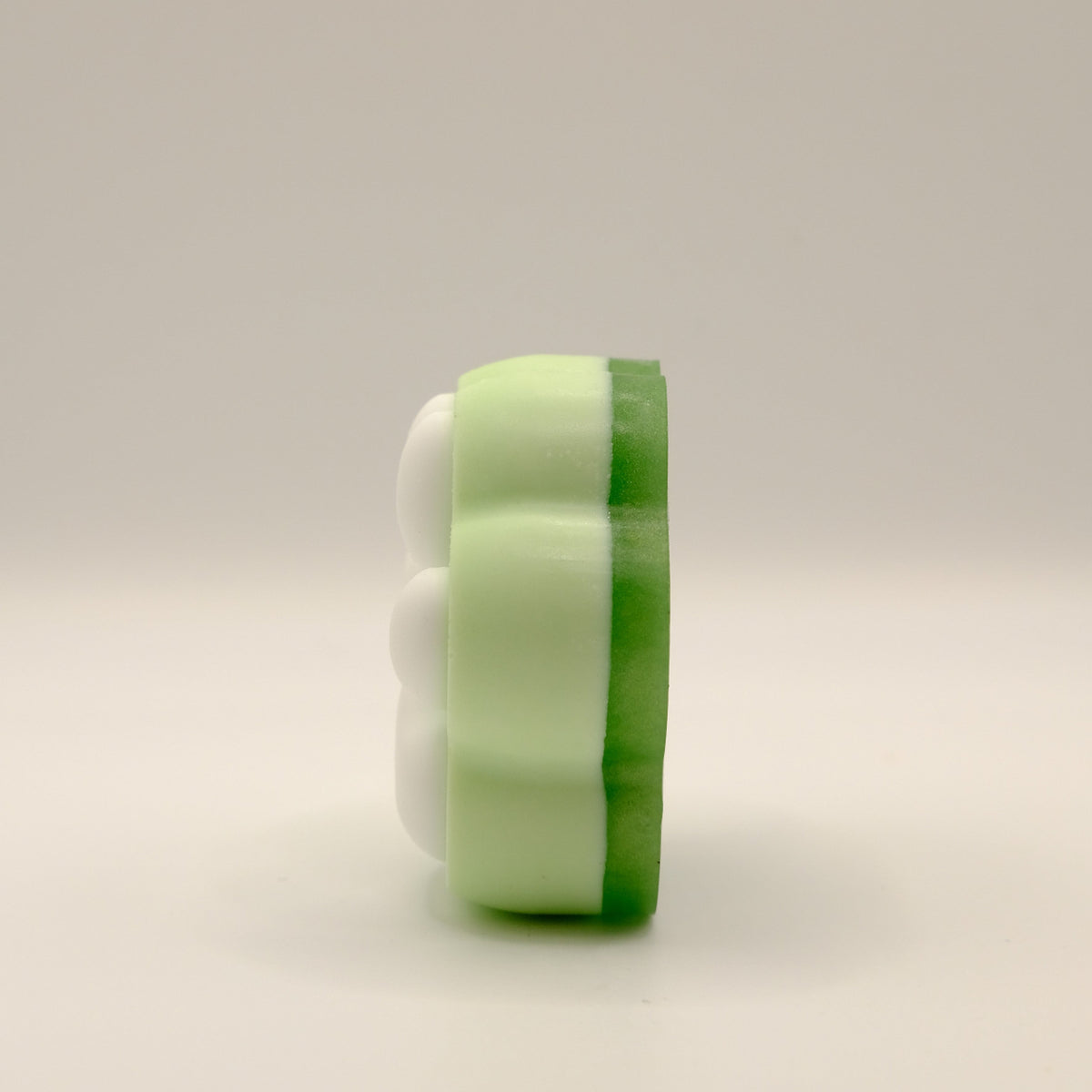 Side view of a green and white soap bar with a paw print design on a light gray background