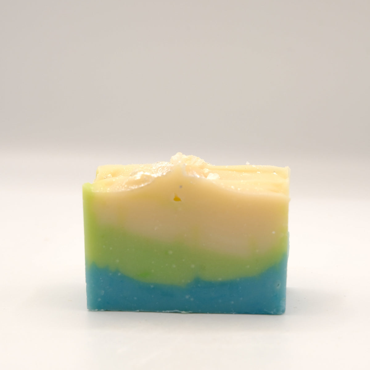 Three-layered soap bar with green, beige, and blue colors on a white background