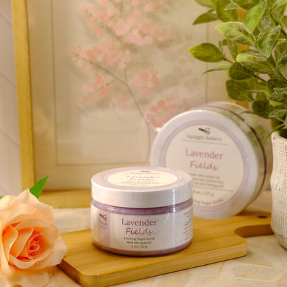 Lavender Fields sugar scrub on a wooden tray, styled with a peach rose and a potted green plant against a warm, neutral background.