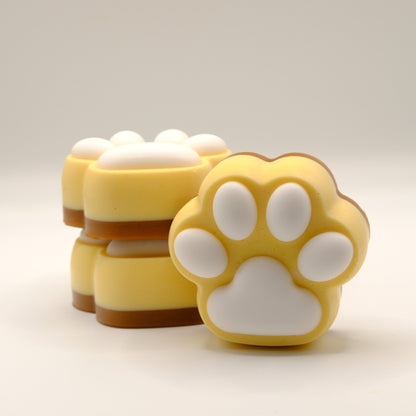 Three brown, yellow and white soap bars with a paw print design on a light gray background