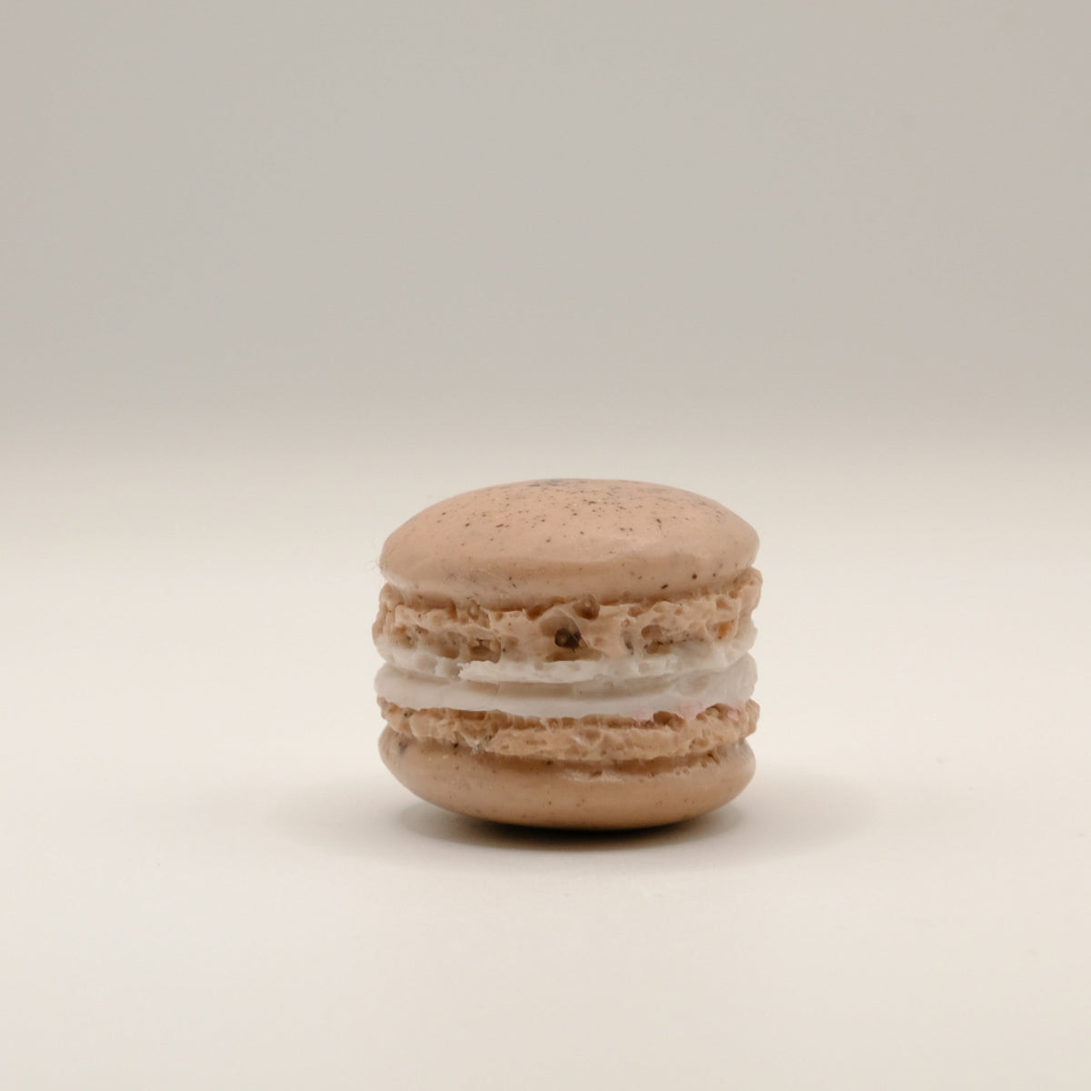 Macaron-shaped soap bar with brown shell and white filling on a beige background