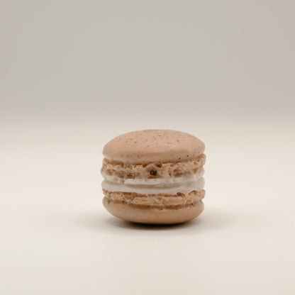 Macaron-shaped soap bar with brown shell and white filling on a beige background