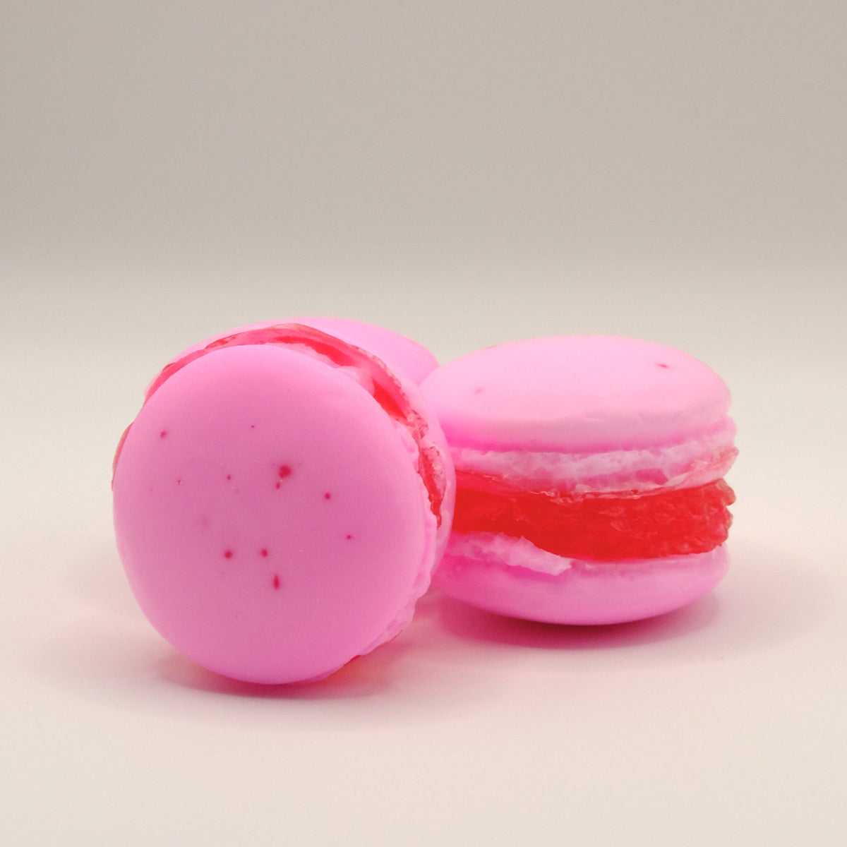 Three pink macaron-shaped soaps with a red filling on a light beige background