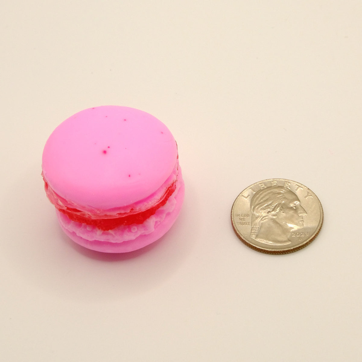 Pink macaron-shaped soap with red filling next to a quarter on a beige background