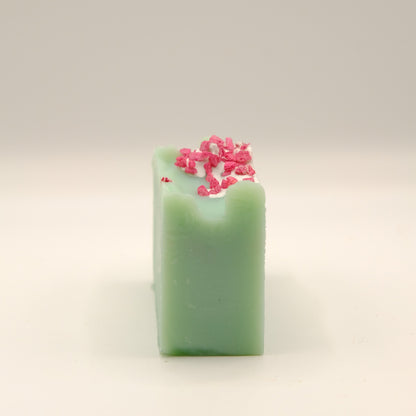 Green soap bar with pink decorative elements on a light beige background