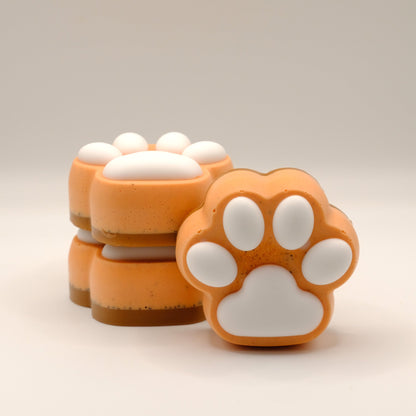 Three orange and white paw-shaped soap bars on a beige background