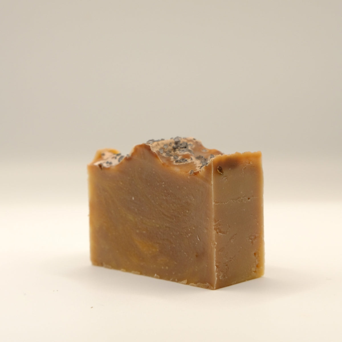 Brown bar of soap with specks and textured top on a beige background