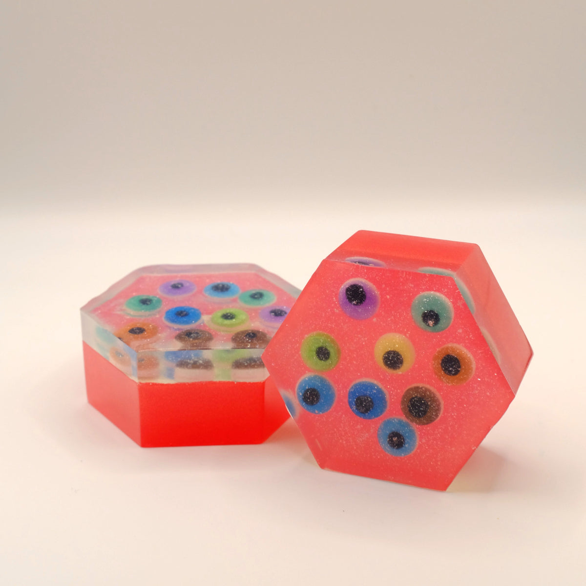 Hexagonal red soap bars with colorful eye-shaped designs on a beige background