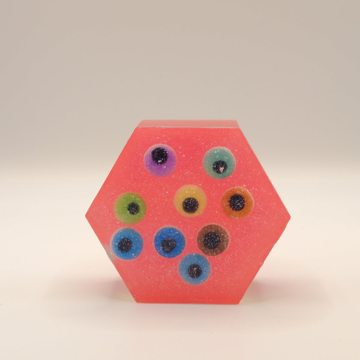 Hexagonal red soap bar with colorful eye-shaped designs on a beige background