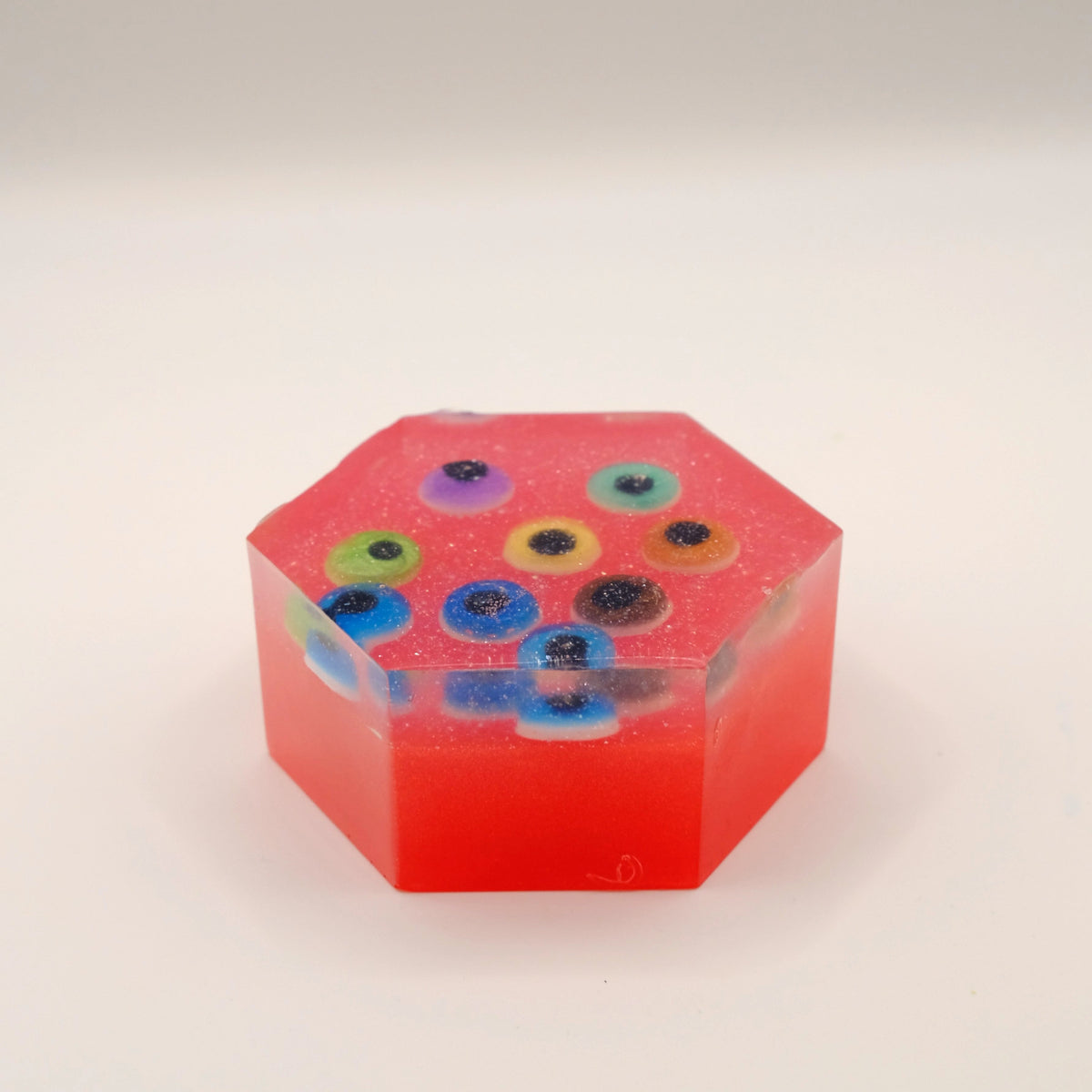Hexagonal red soap bar with colorful eye-shaped designs on a beige background