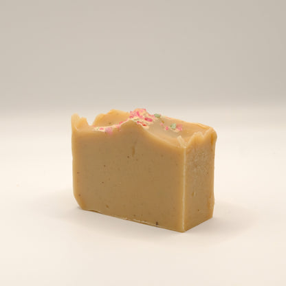 Light brown bar of soap with pink specks on top all on a light background