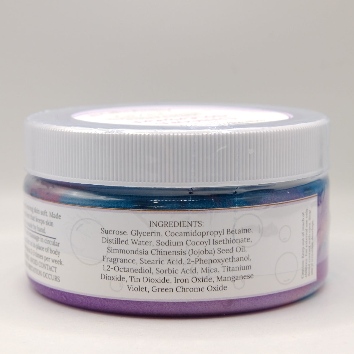 Jar of purple and blue sugar scrub with a white lid on a light gray background
