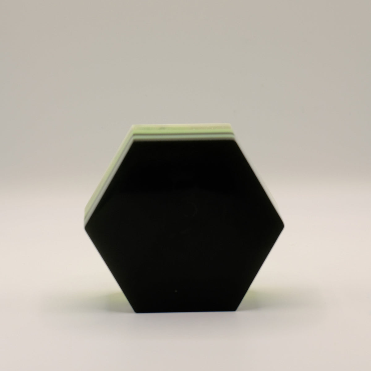 Hexagonal black soap bar with a green top on a light gray background
