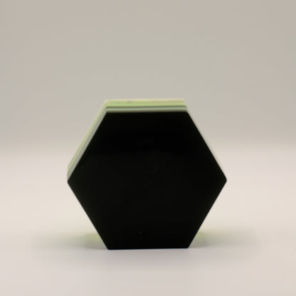 Hexagonal black soap bar with a green top on a light gray background
